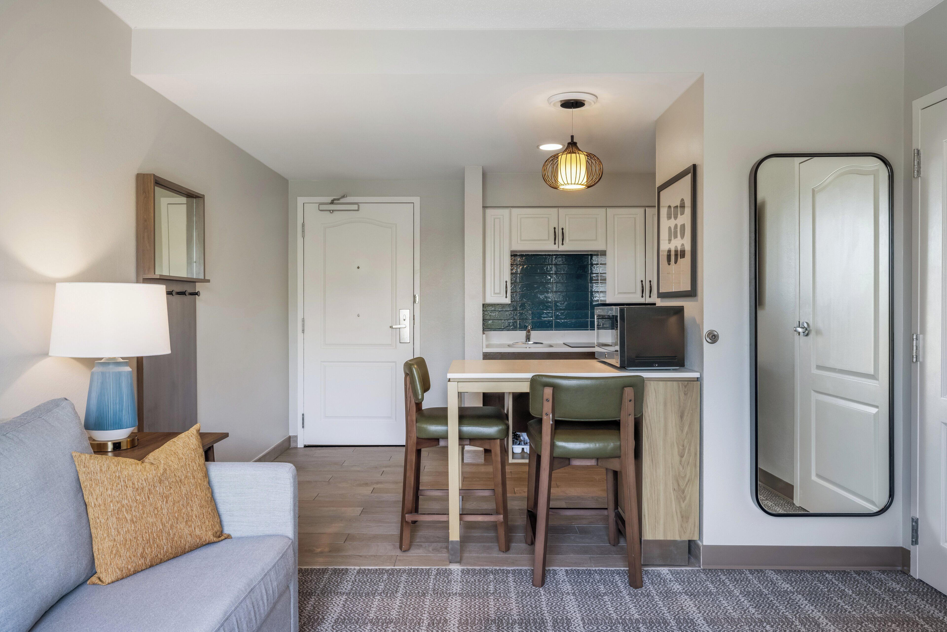 A compact living space with a dining area, kitchenette, and a sofa with a lamp.