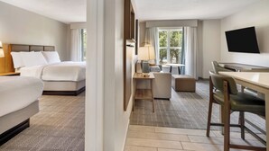 Ein Hotelzimmer mit Bett, Schreibtisch, Sessel, Fernseher und Fenster.