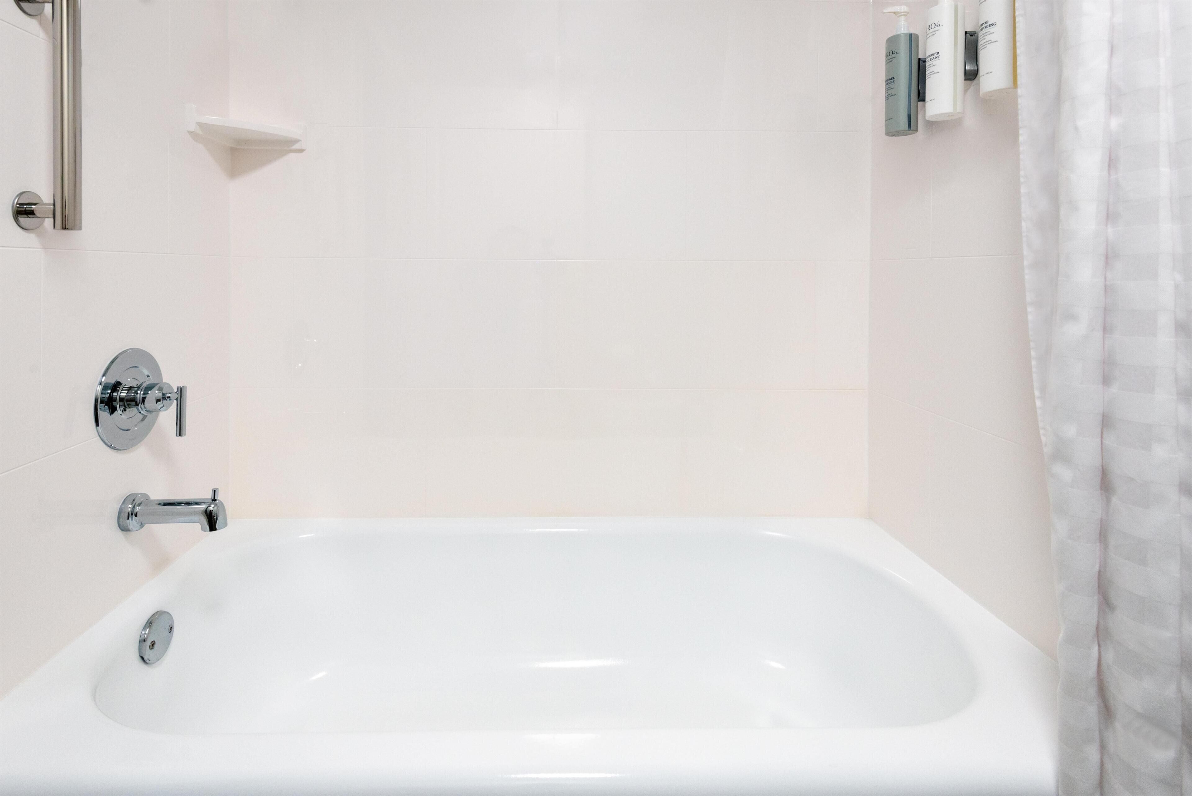 Una bañera blanca con grifería cromada, un cabezal de ducha y un estante pequeño en la pared.