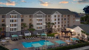 A hotel with multiple floors, a swimming pool, outdoor seating, and palm trees.