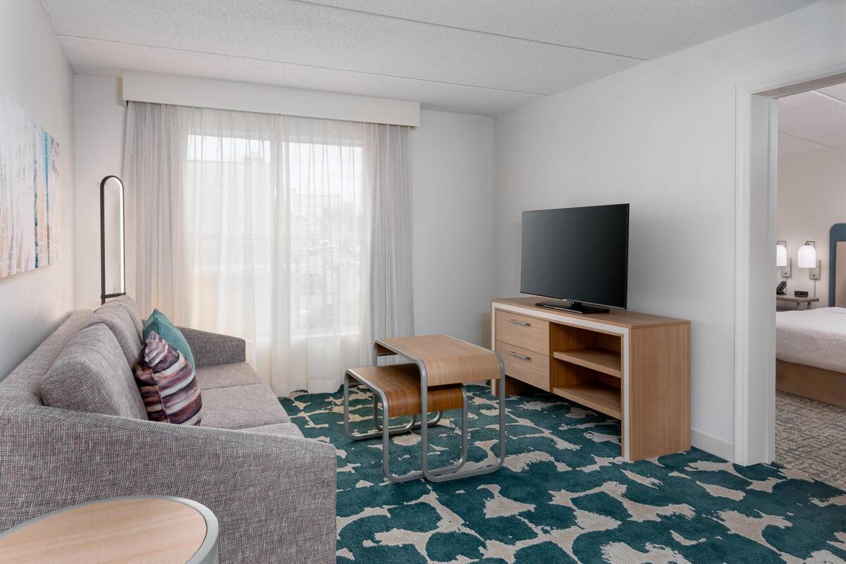 Une chambre d’hôtel avec un canapé, un téléviseur posé sur un meuble en bois, un bureau et un lit.