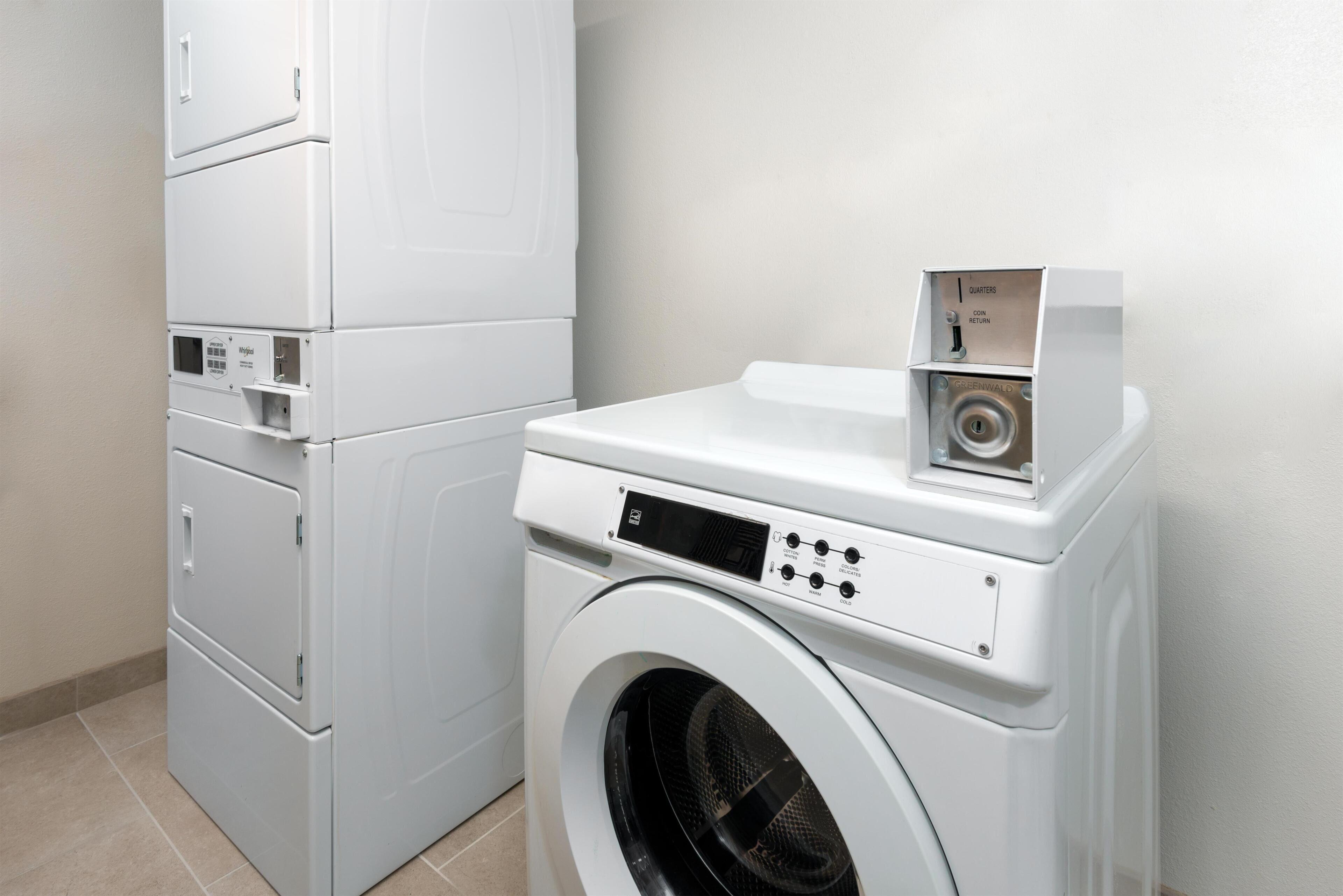 A compact laundry area with a front-loading washing machine and stacked dryers.