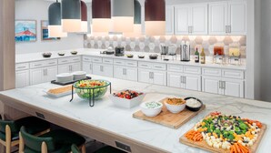 A modern kitchen with white cabinets, a marble countertop, and a variety of food items displayed.