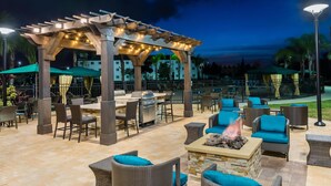 An outdoor patio with wicker furniture, a barbecue grill, and a pergola with string lights.