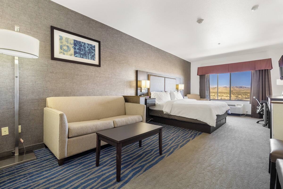 A hotel room with a bed, a sofa, a desk, and a large window with a view of the desert.