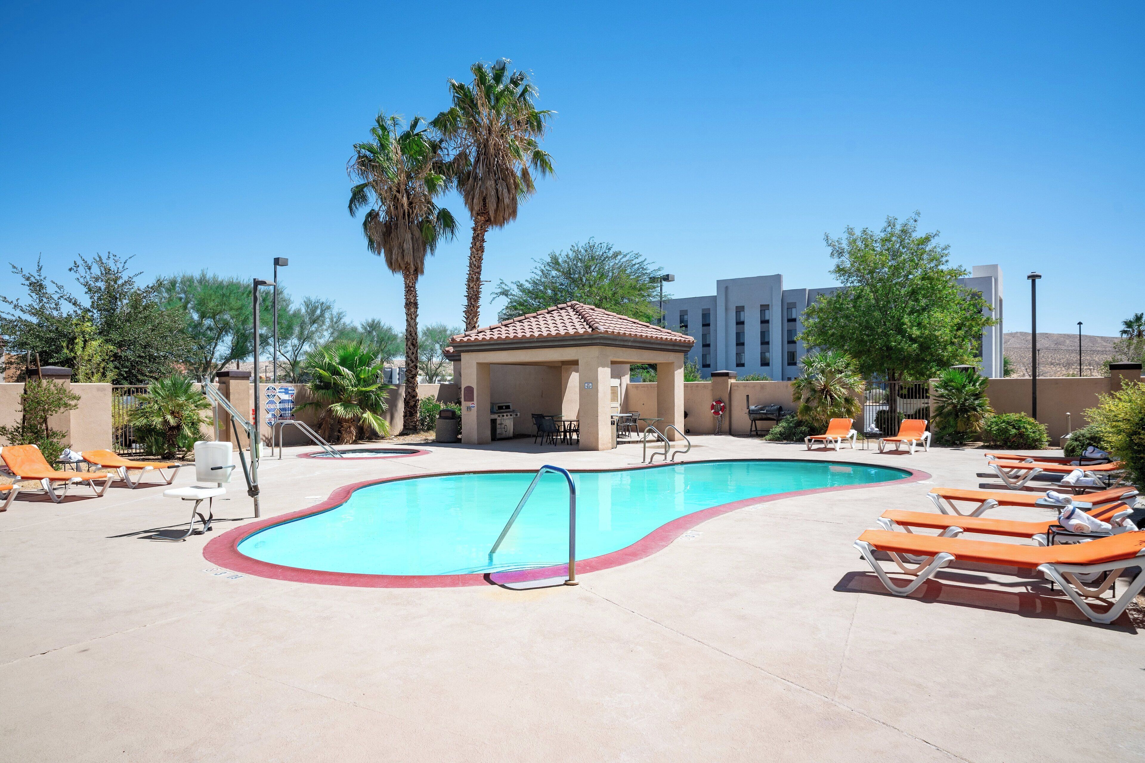 A swimming pool with lounge chairs, a small pavilion, and palm trees.