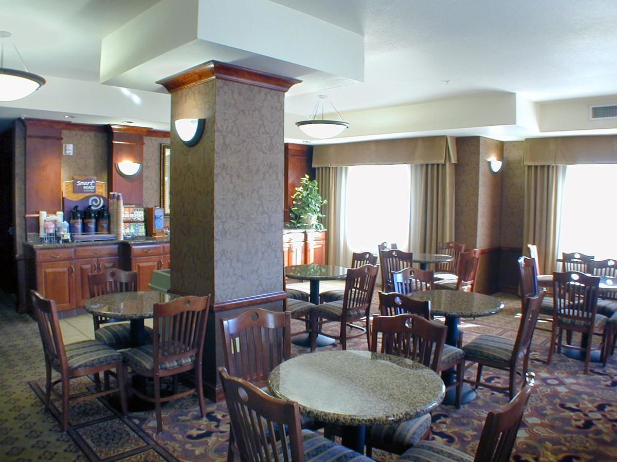 A hotel dining area with multiple round tables and chairs, a bar area with a cash register, and a large pillar.