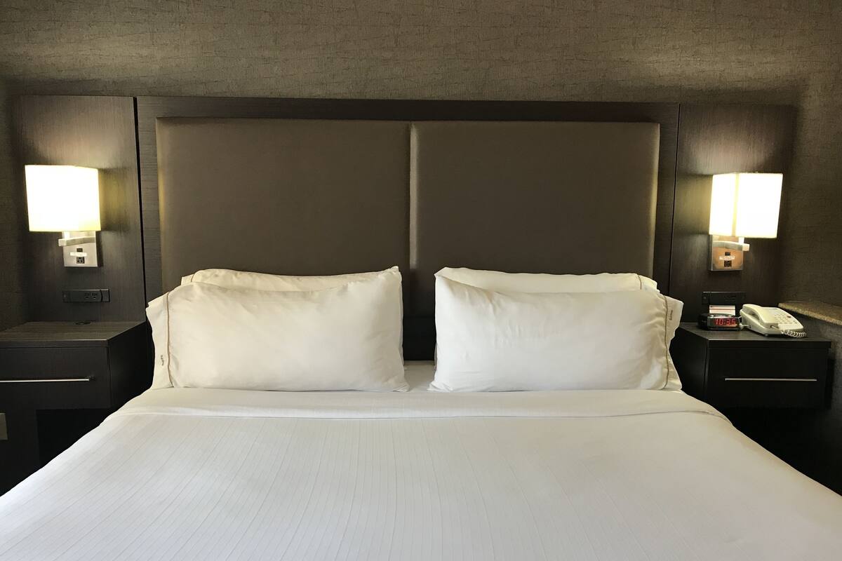 A hotel room with a large bed, two bedside lamps, a nightstand, and a phone.