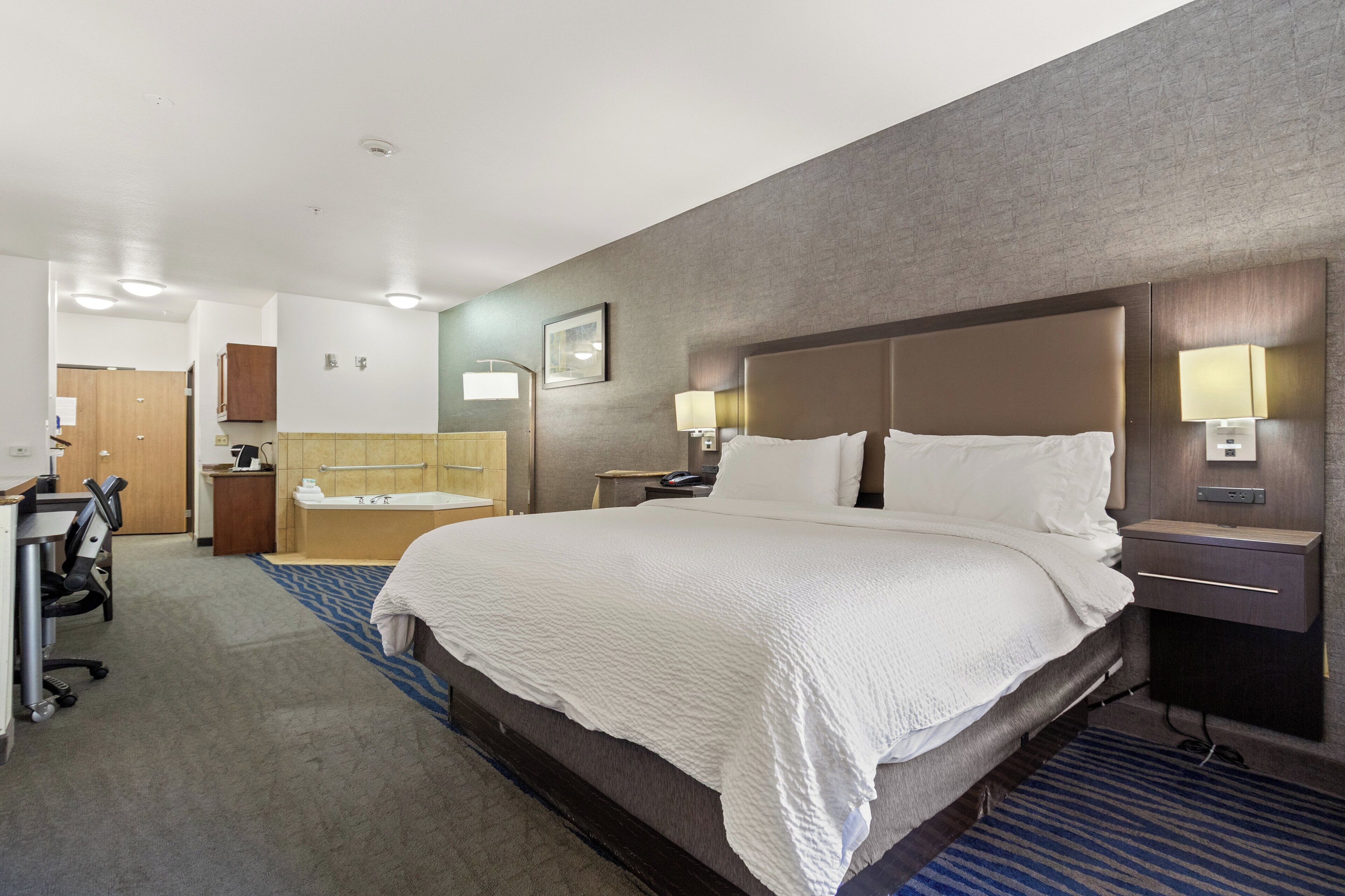 A hotel room with a large bed, a desk, a chair, a bathroom with a bathtub, and a mirror.