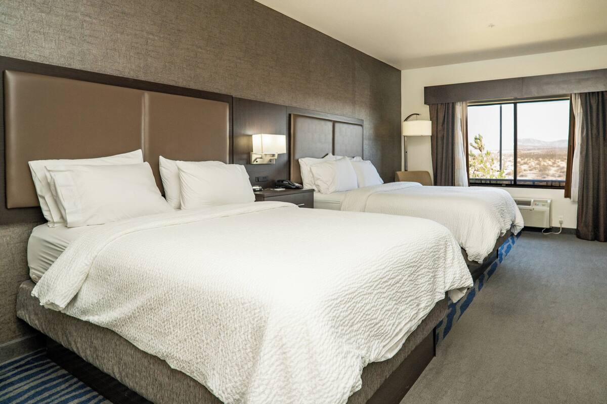 A hotel room with two beds, a large window, and a view of the desert.