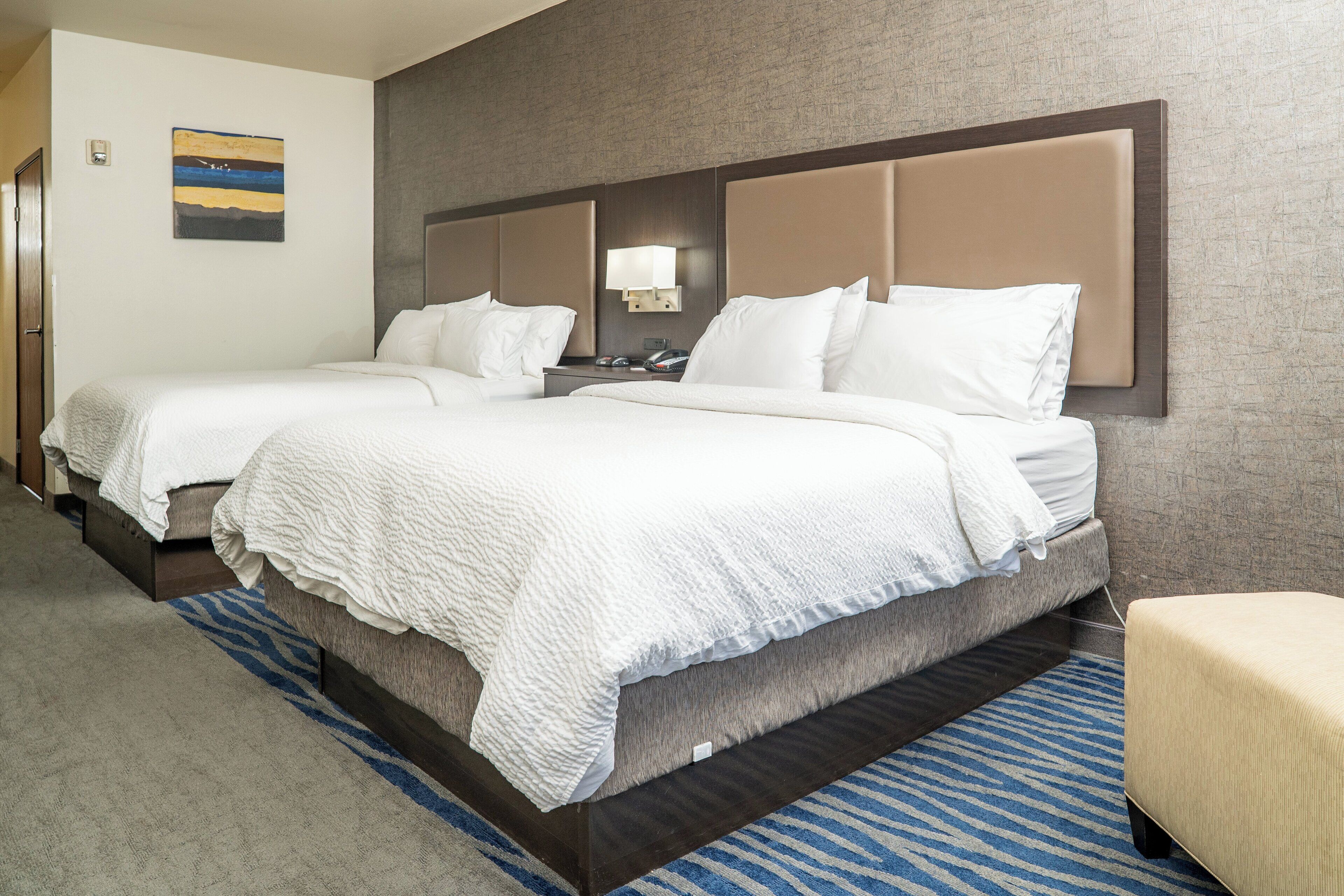 A hotel room with two beds, a nightstand, a lamp, and a blue patterned rug.