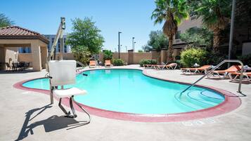 Un espace piscine avec des chaises longues, un poste de surveillance pour le sauveteur et un bâtiment en arrière-plan.