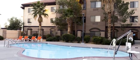 A Holiday Inn Express & Suites with a swimming pool, orange lounge chairs, and palm trees.