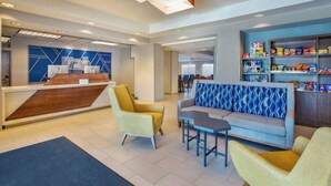 A hotel lobby with a reception desk, seating area, and snack bar.