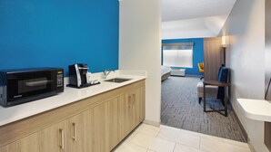 A compact hotel room with a kitchenette, a bed, a small table, and a chair.
