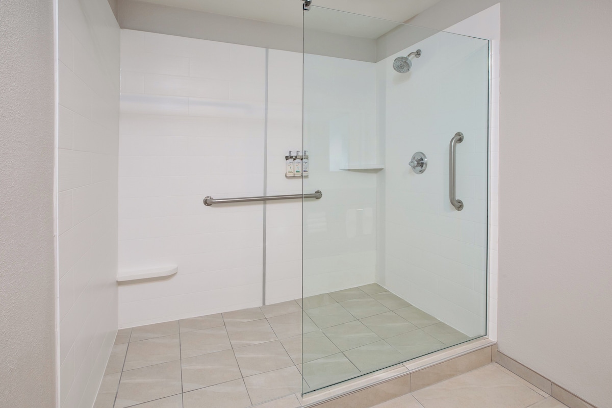A glass-enclosed shower with a handrail, a control panel, and a tiled floor.