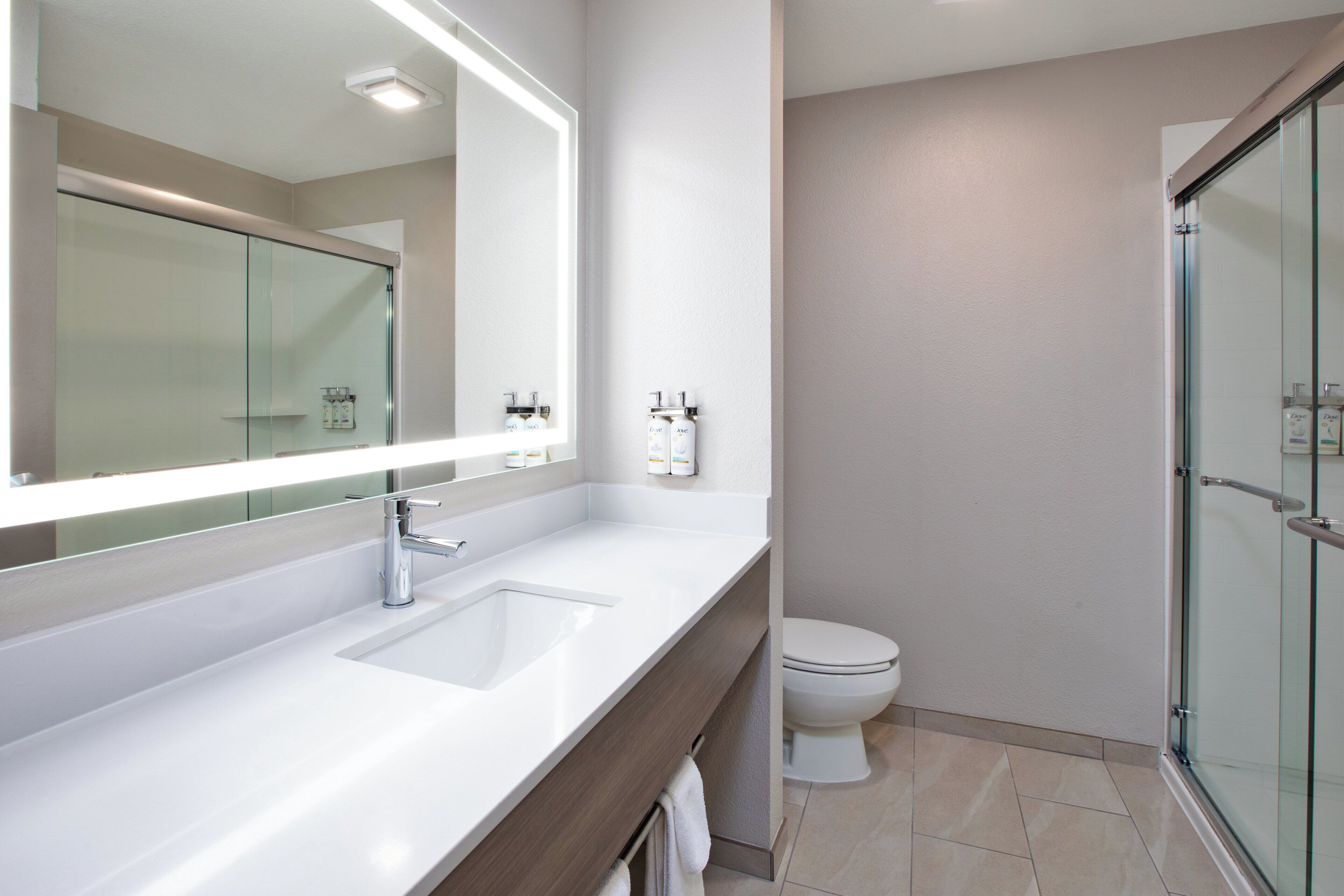 A modern bathroom with a large mirror, a sink, a toilet, and a glass shower enclosure.