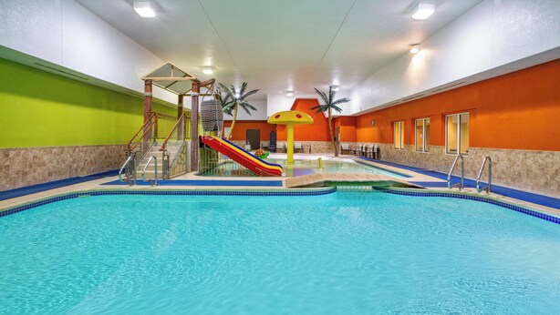 An indoor swimming pool with a slide, palm trees, and a play structure.