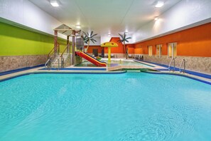 An indoor swimming pool with a slide, palm trees, and a play structure. - Holiday Inn Express Fremont by IHG (Fremont)