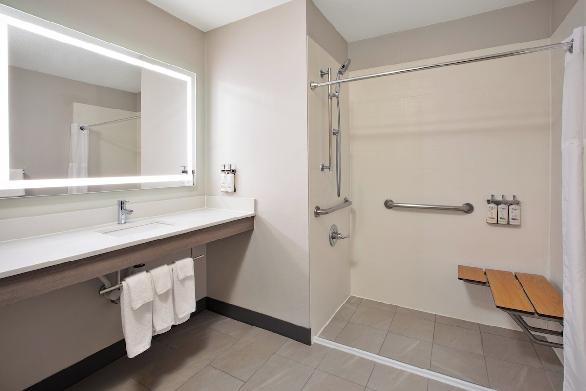 A modern bathroom with a large mirror, a sink, a shower with a glass door, and a bench.