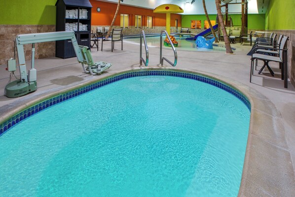 An indoor swimming pool with a clear blue water, a lifeguard stand, and a children's play area with slides.