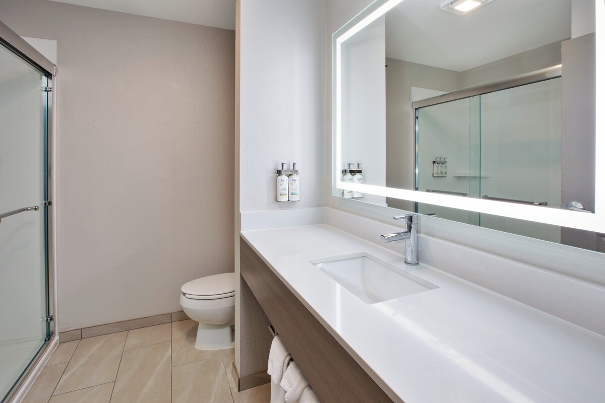 A modern bathroom with a glass shower enclosure, a white toilet, and a vanity with a large mirror and two sinks.