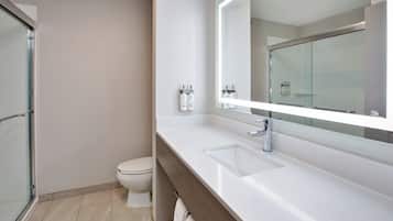 A modern bathroom with a glass shower enclosure, a white toilet, and a vanity with a large mirror and two sinks.