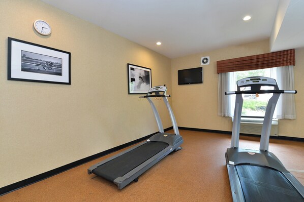 A gym with two treadmills, a wall clock, and two framed pictures.