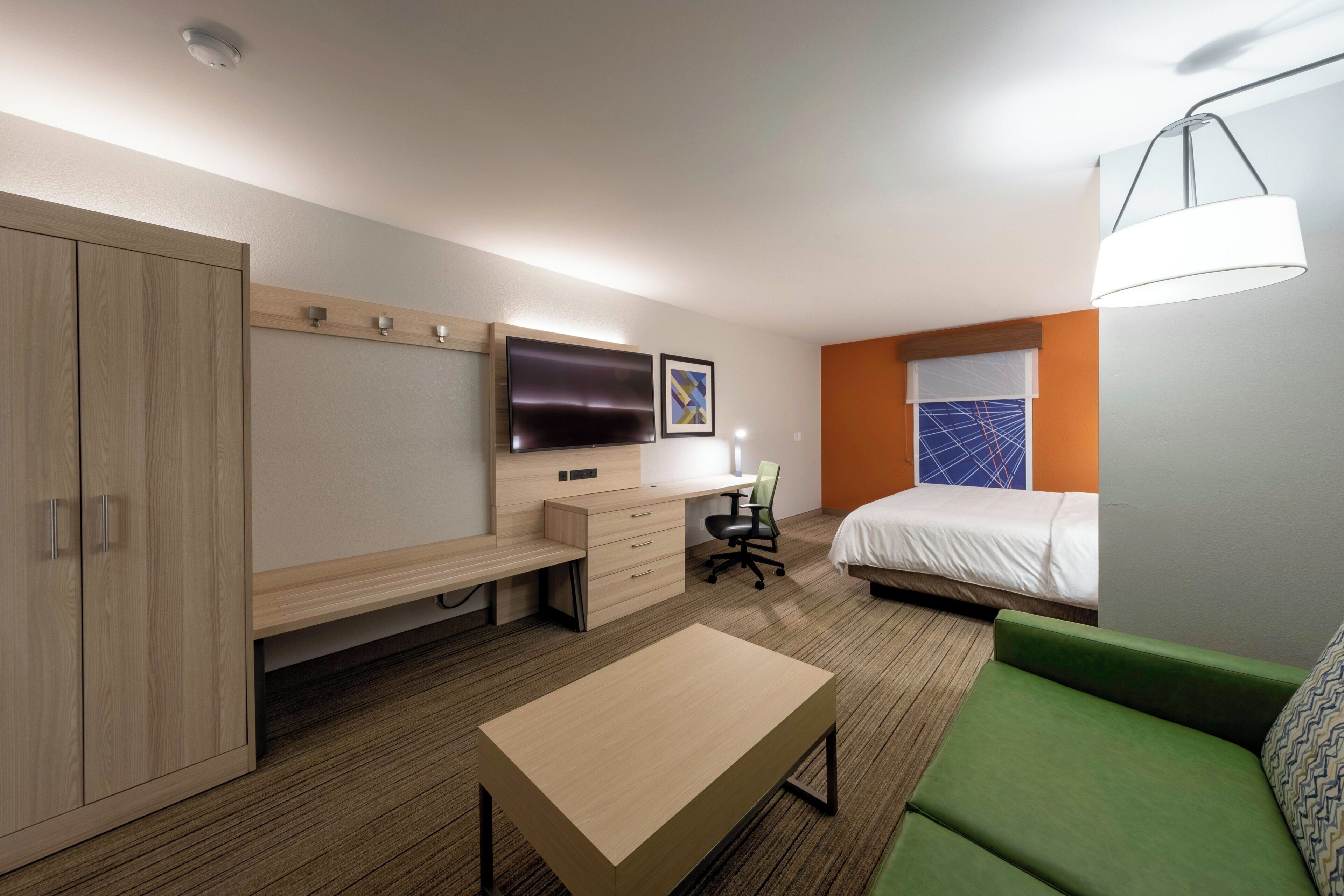 Habitación de hotel con cama, escritorio con silla, televisor, armario y sofá verde.