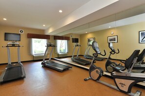 Une salle de sport équipée de tapis de course, de vélos d’appartement et d’un téléviseur.