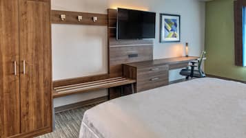 Habitación de hotel con una cama grande, un armario de madera, un escritorio con una silla, un televisor de pantalla plana montado en la pared y una obra de arte abstracta enmarcada.