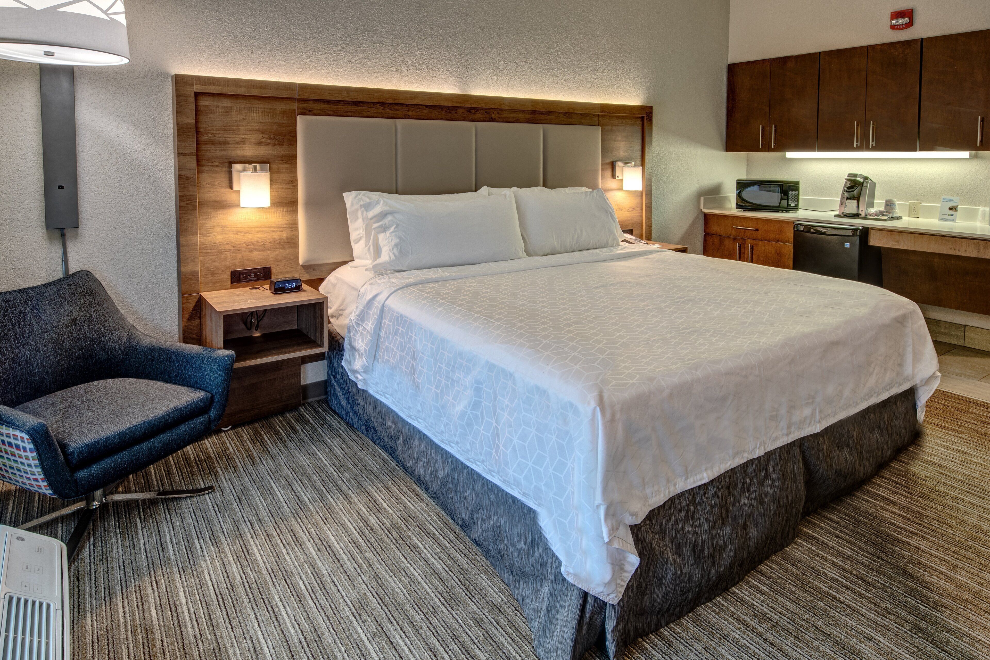 A hotel room with a large bed, a chair, a desk with a lamp, a microwave, and a coffee maker.