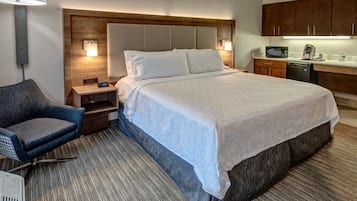 Une chambre d’hôtel avec un grand lit, une chaise, un bureau avec une lampe, un four à micro-ondes et une machine à café.