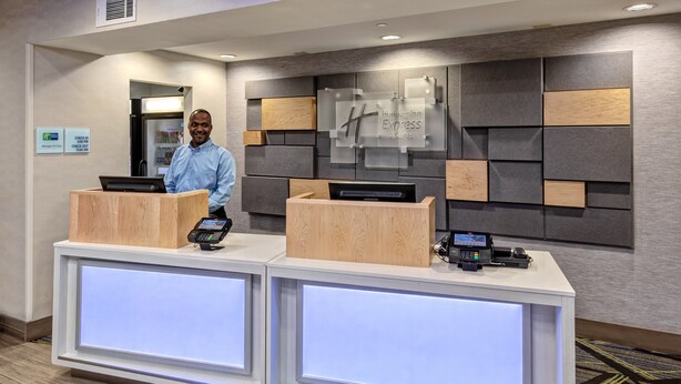 A hotel reception desk with two counters, a digital screen, and a sign indicating check-in/out times. - Holiday Inn Express Hotel & Suites Memphis Southwind by IHG (Memphis)