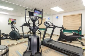 Un gimnasio con diversos equipos de ejercicio, incluyendo cintas de correr y bicicletas estáticas, un televisor montado en la pared y un espejo que refleja los equipos.
