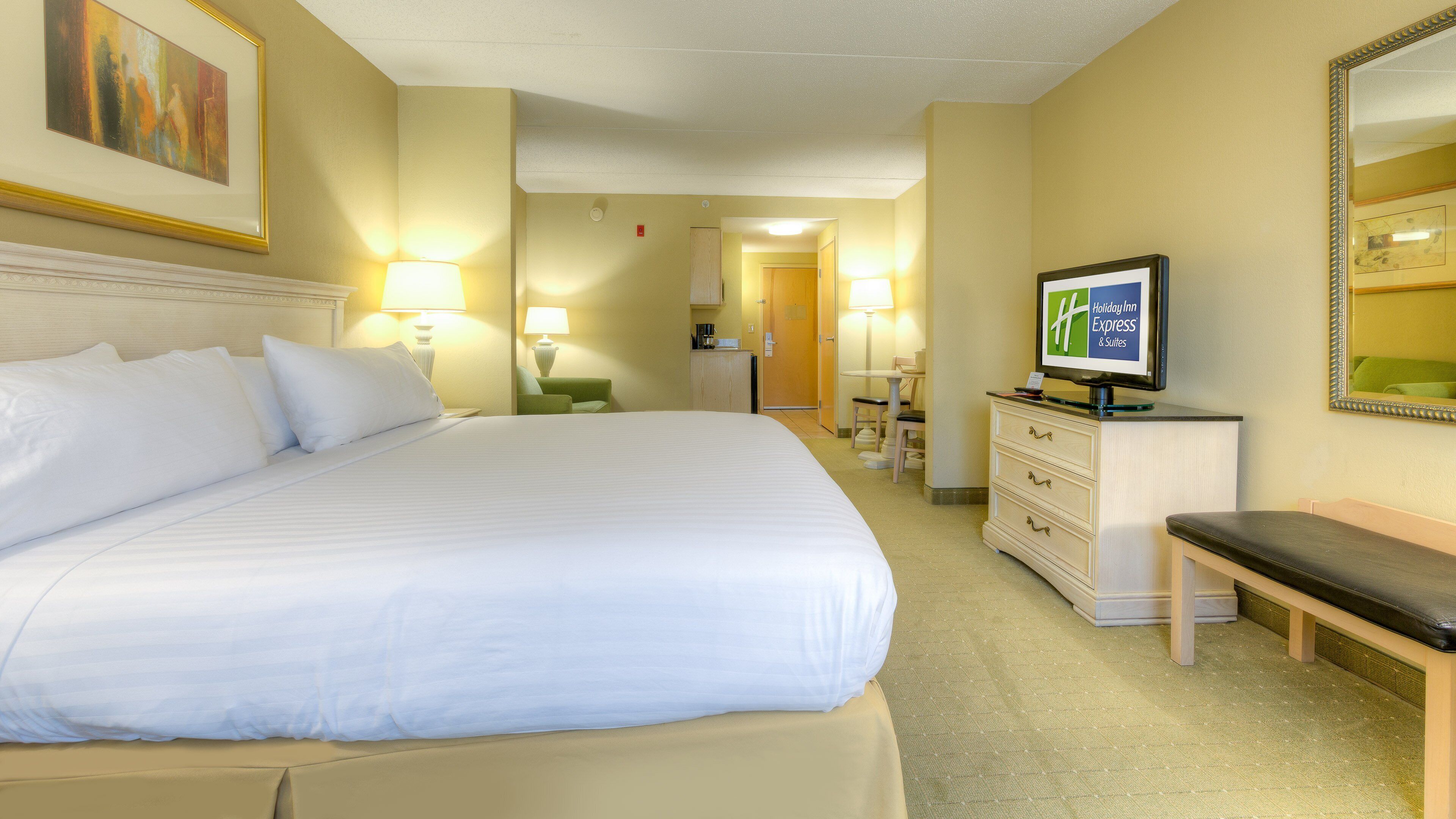 A hotel room with a large bed, a desk with a computer, a chair, a dresser, and a television.