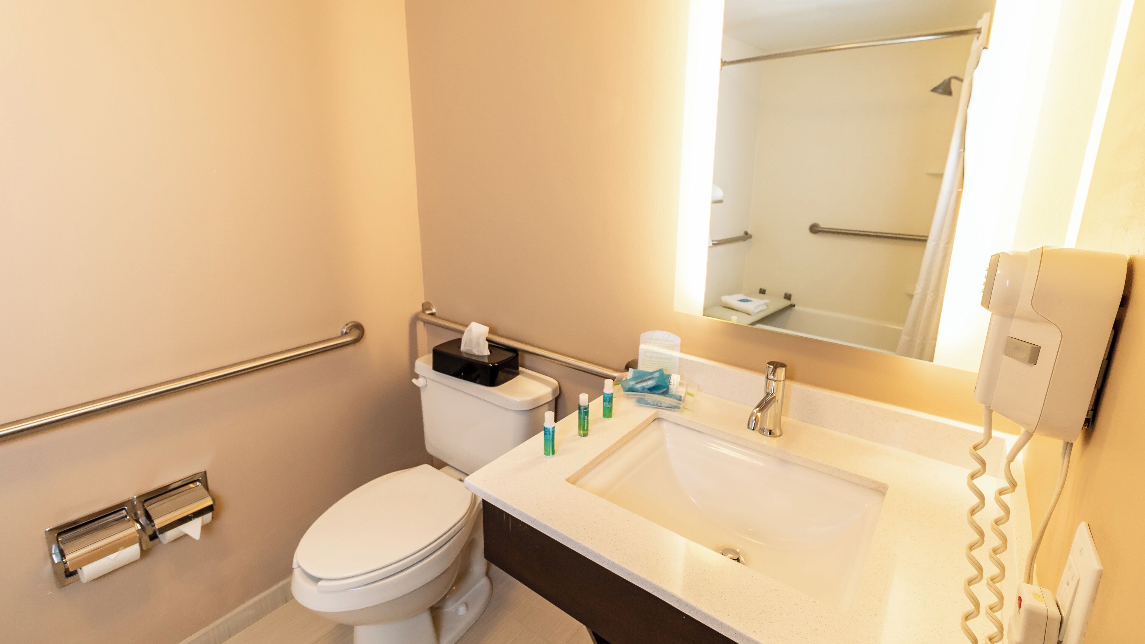 A bathroom with a toilet, sink, mirror, and hand dryer.
