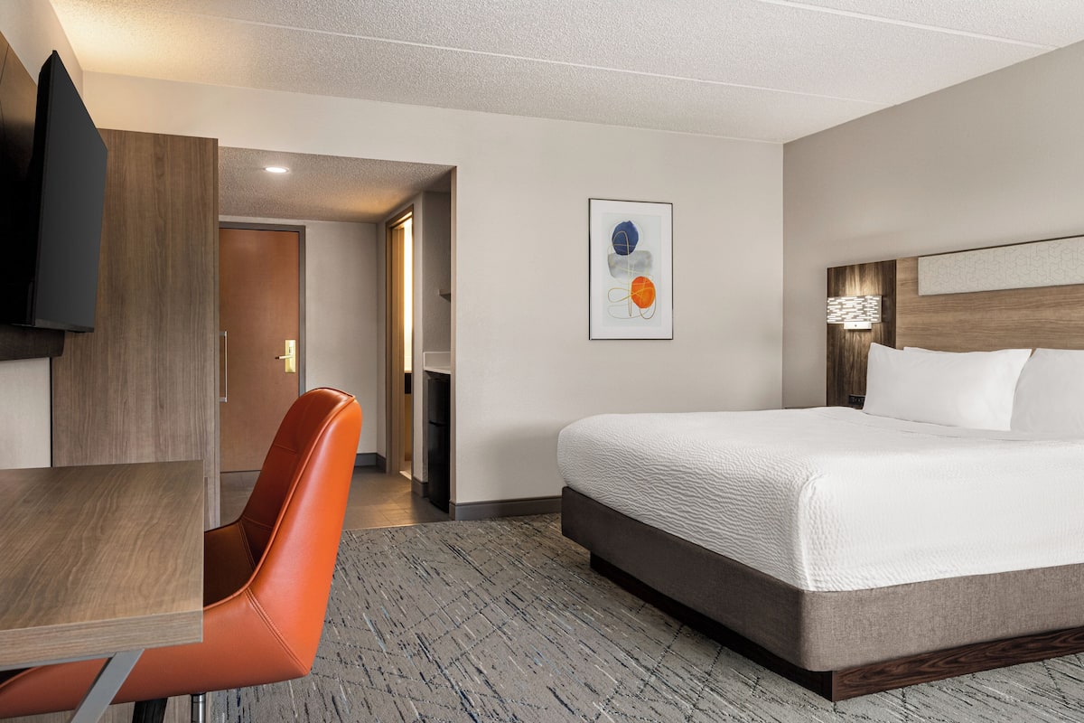 A hotel room with a bed, a desk, a chair, and a television.