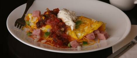 Un plato blanco con huevos revueltos, jamón, queso y una cucharada de crema agria sobre una superficie oscura.