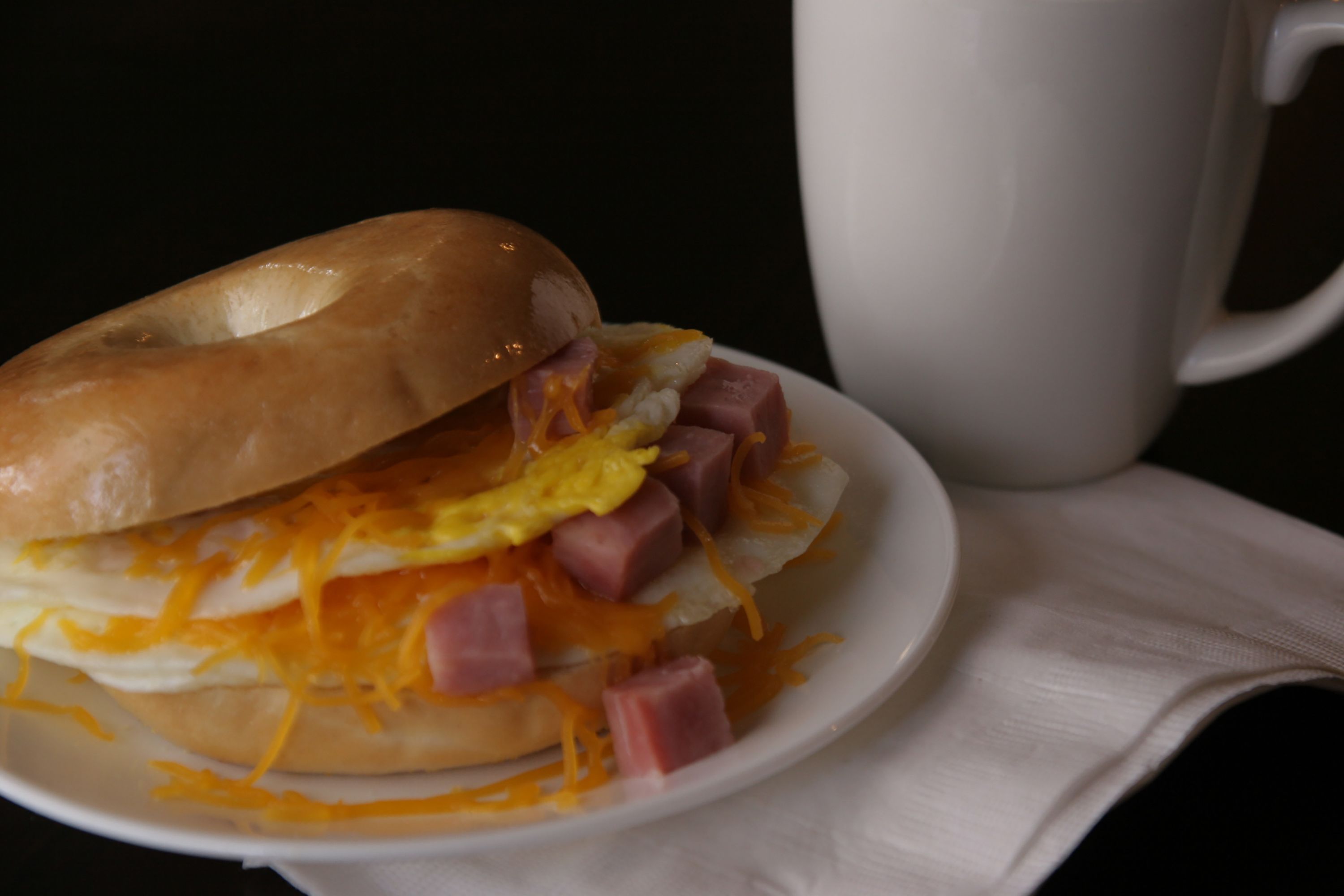 A breakfast sandwich on a plate with a white mug in the background.