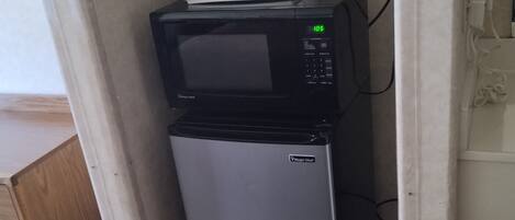 A compact kitchenette with a microwave and a small refrigerator, a coffee maker, and a cup of coffee on the counter.