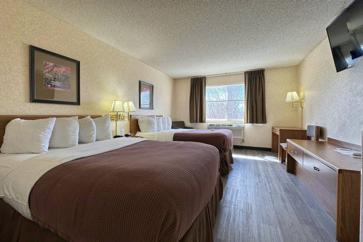A hotel room with two beds, a desk, a chair, a TV, and a window with curtains.