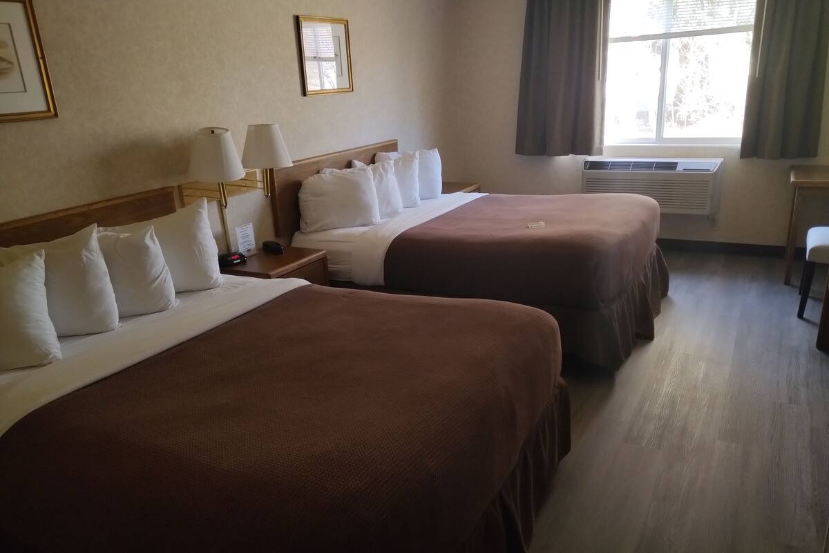 A hotel room with two beds, a desk, a chair, and a window with curtains.