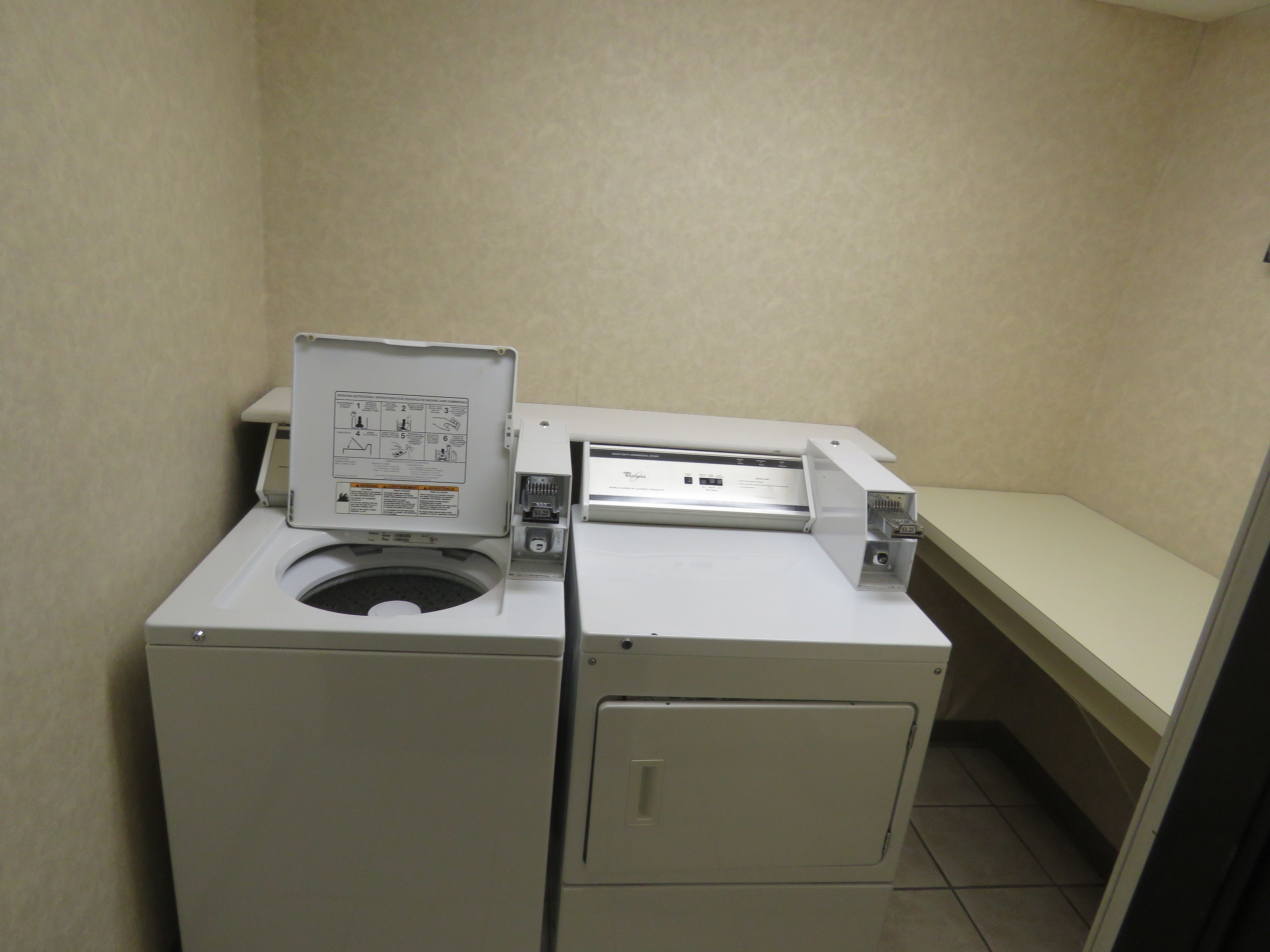 Uma lavanderia compacta com máquina de lavar e secadora frontais, uma pequena mesa e uma prateleira fixada na parede.
