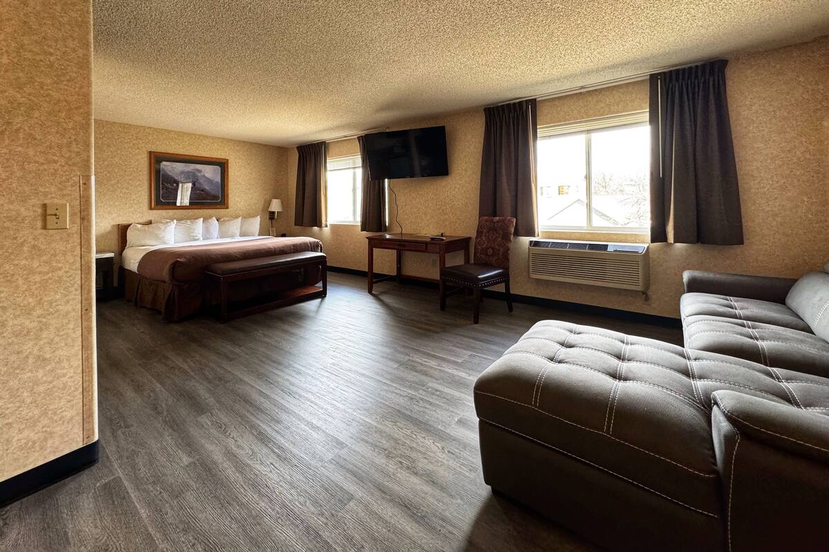 A hotel room with a bed, a sofa, a desk, and a TV mounted on the wall.