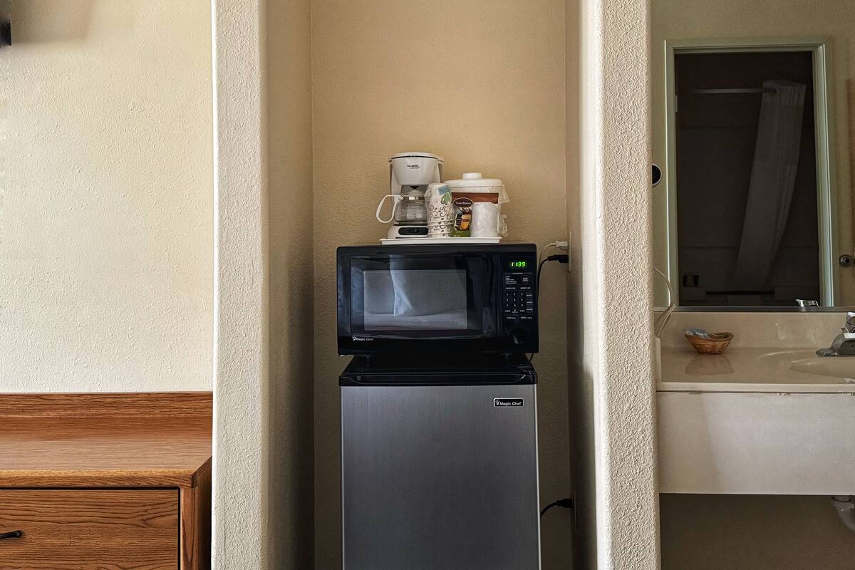 A compact kitchenette with a microwave on top of a refrigerator, a coffee maker, and a small basket.