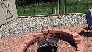 A circular fire pit surrounded by a brick border, set in a gravel area with a grassy background. - Stay Wise Inn Cedaredge (Cedaredge)