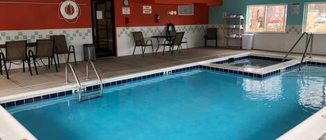 Una piscina interior con borde de azulejos, una silla de salvavidas y una puerta con señal de salida.