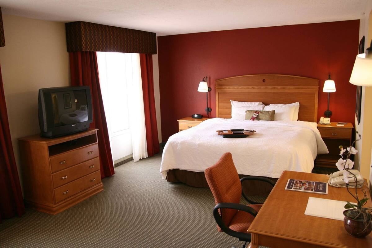 Une chambre d’hôtel équipée d’un lit, d’un bureau, d’une chaise, d’une télévision, d’une table de chevet et d’une lampe.