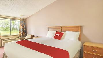 A hotel room with a large bed, a wooden nightstand, a bedside table, and a window with curtains.